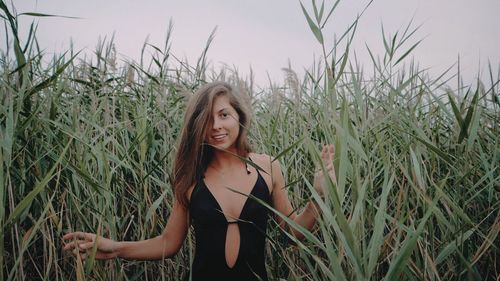 Portrait of smiling beautiful woman standing on field against cereal plants