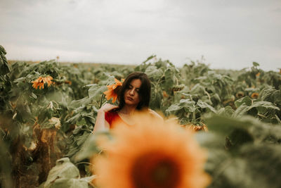 Woman standing amidst sunflower plants against sky