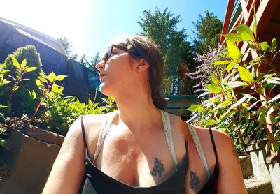 Young woman wearing sunglasses standing against plants