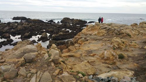 Distant view of couple standing at rocky shore