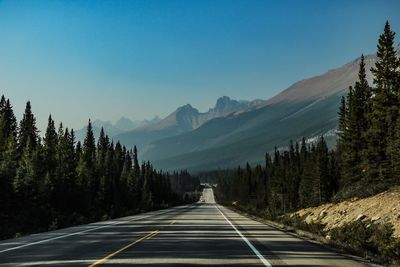 Road leading towards mountains against clear sky