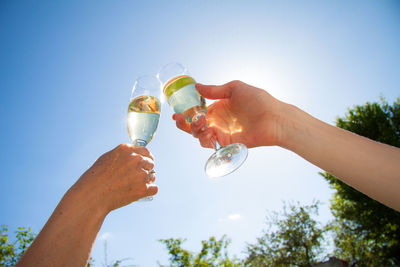 Cropped image of hand toasting champagne flutes against sky