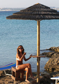 Portrait of woman wearing bikini while sitting on rocky shore