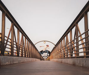 Young man jumping on footbridge against clear sky during sunset