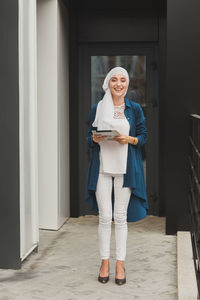 Smiling young woman holding digital tablet standing outdoors