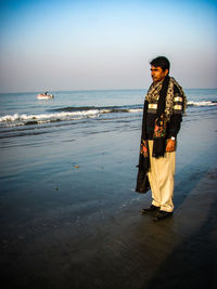 Full length of thoughtful man standing on shore against sky at beach