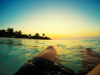 Low section of man on beach against sky during sunset