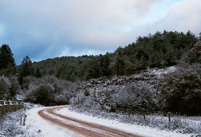 Road by hills against cloudy sky during winter