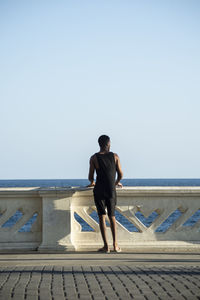 Rear view of man standing on sea shore against clear sky