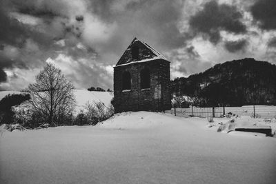 House on field by building against sky during winter