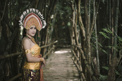Portrait of woman wearing traditional clothing standing on boardwalk amidst trees