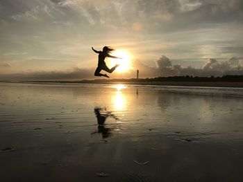 Silhouette woman jumping at beach against sky during sunset