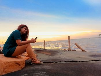 Full length of woman sitting on beach against sky during sunset