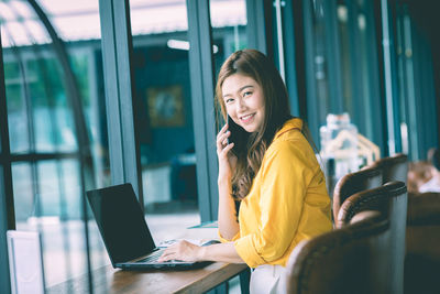 Young woman using phone while sitting on table