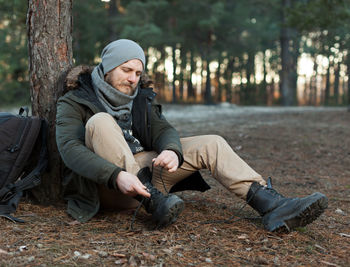 Young man sitting by trees in forest