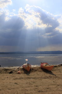 Kayaks moored at beach against cloudy sky on sunny day