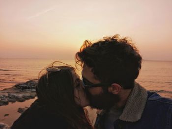 Close-up of couple kissing against sea during sunset