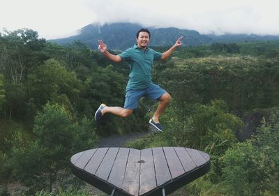 Portrait of excited man jumping on heart shape platform over trees in forest