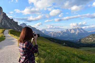 Rear view of woman photographing on mountain against sky