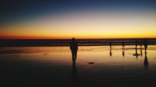 Silhouette people standing on beach during sunset