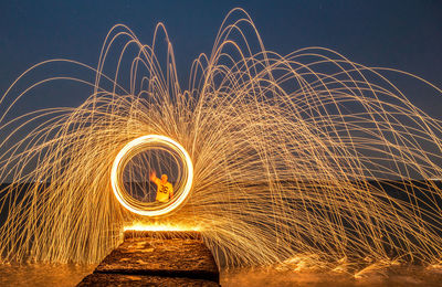 Full length of man spinning wire wool on pier by sea at night