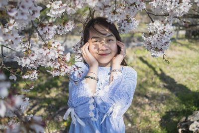 Portrait of smiling young woman standing by cherry blossom tree