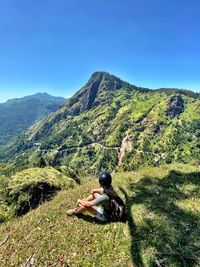 Man sitting on mountain against sky