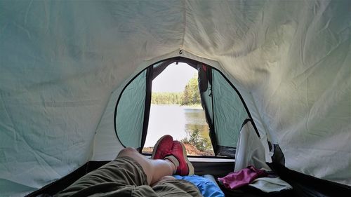 Low section of man relaxing in tent at lakeshore