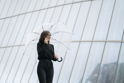 Woman holding umbrella standing against built structure