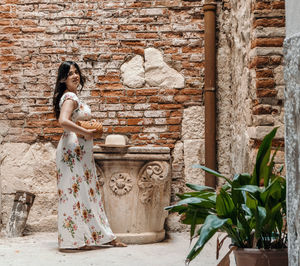 Full length portrait of beautiful woman in summer style dress, standing in front of brick wall