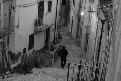 Rear view of man walking on staircase amidst buildings in city 