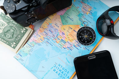 High angle view of map with camera and mobile phone on white background