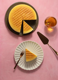 From above plates with tasty cotton cheesecake placed near glass of beverage on pink background