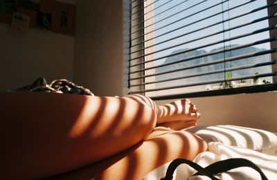 Low section of young woman resting on bed at home