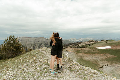 Engaged couple in all black embrace hug on windy ridge top in wyoming