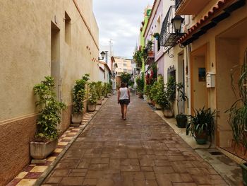 Rear view of woman walking on footpath amidst buildings