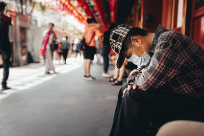 Side view of man wearing pollution mask while sitting on seat in city