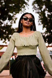 Portrait of a young woman wearing light green blouse, black skirt and sunglasses and hoop earrings