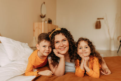 A happy mother hugs her children a little boy and a girl in pajamas sitting on bed in cozy interior 
