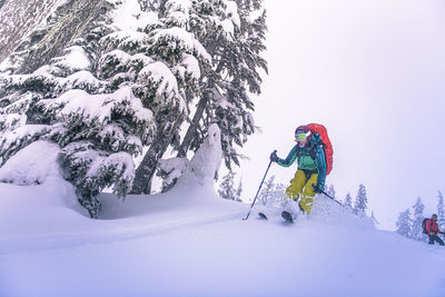 Woman jumping from top of snowy hill while backcountry skiing in bc