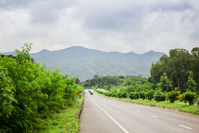 Empty road along trees and mountains against sky