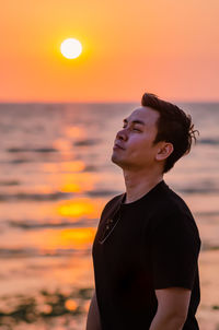 Asian man looking up to sky with sunset at the beach background. positive mental health.