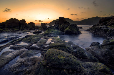 Rocks on shore against sky during sunset