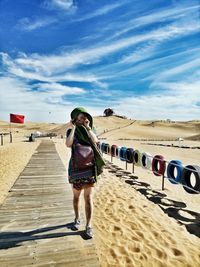 Portrait of woman wearing eyeglasses while walking on wooden walkway at beach