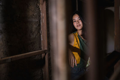 Portrait of smiling young woman standing against wall seen through metal