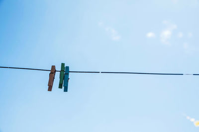 Low angle view of clothespins hanging on rope against blue sky