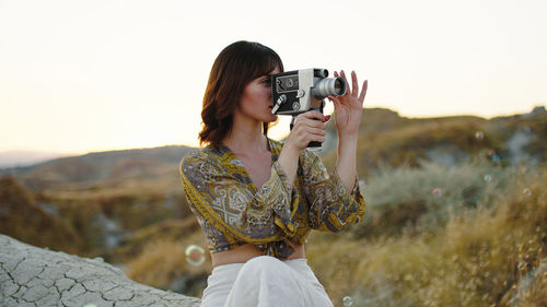 Young girl shoots with the 8mm vintage camera in the nature among the bubbles