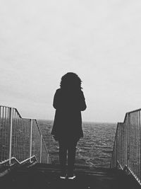 Rear view of woman standing on railing against sky