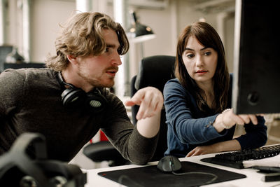 Female professional showing computer to coworker at workplace