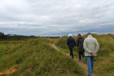 Rear view of people walking on field against sky